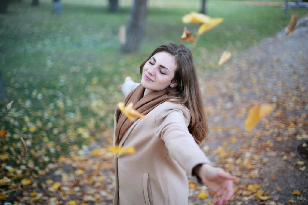 woman in the park with winter leaves falling down on her